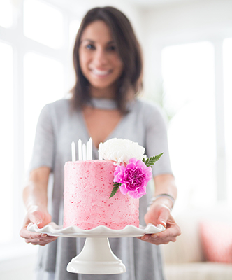 pretty young woman presenting pink birthday cake with flowers