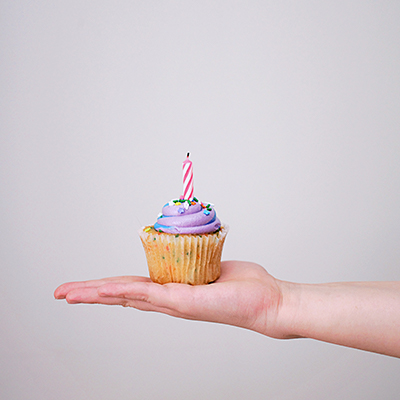 outstretched hand with cupcake with purple icing and one birthday candle